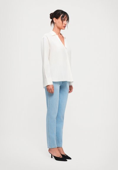 Cămașă albă cu mâneci lungi și guler, asociată cu blugi drepți de culoare albastră deschisă și pantofi cu vârful ascuțit de culoare neagră; design elegant și textură fină.
