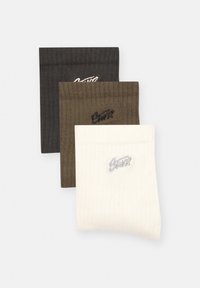 Tre par ribbede sokker i sort, olivengrøn og hvid, hver med broderet logo ved kanten, med en glat tekstur.