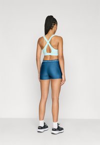 Ανοιχτό μπλε αθλητικό σουτιέν με σχεδιασμό πίσω με σταυρωτές λωρίδες, συνδυασμένο με σκούρα μπλε στενά σορτς. Καθαρές γραμμές και ομαλή υφή.