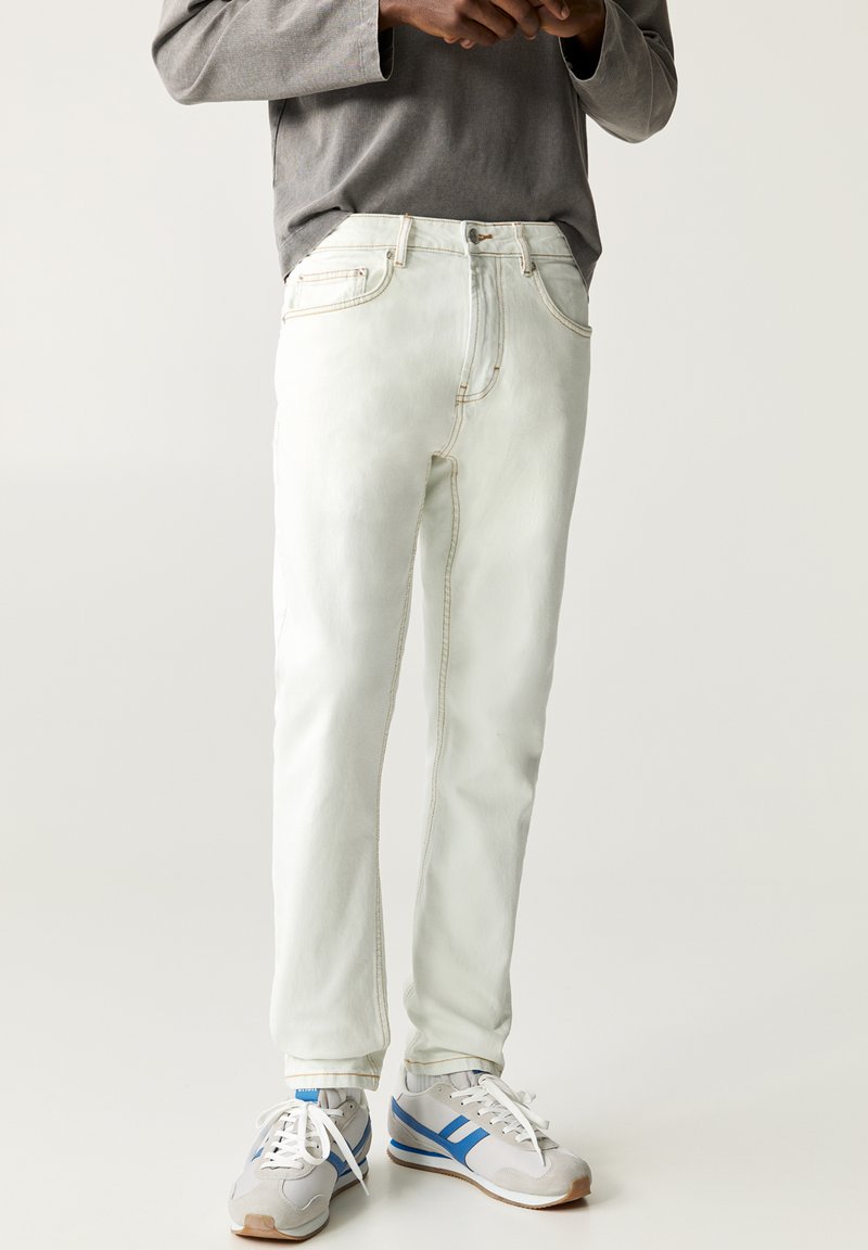 Witte denim jeans met een rechte snit, voorzien van lichte stiksels en twee vo pockets. Gecombineerd met een grijze longsleeve shirt en grijs-blauwe sneakers.