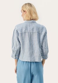 Lyseblå stribet skjorte med en cropped design, lange ærmer optrukket, lavet af et struktureret stof, parret med lyseblå bukser.