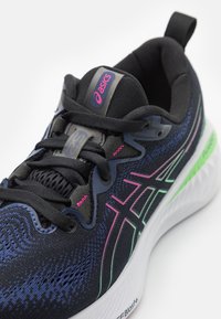 Black athletic shoe with a textured knit upper, neon green and pink accents, and a cushioned sole. Features a lace-up closure and logo tag.