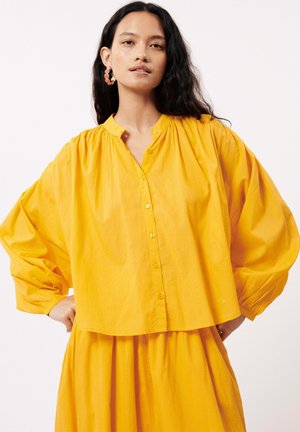 Geel, button-up blouse met een relaxte pasvorm, pouf mouwen en een geplooide halslijn. Textiel met een zachte val, gecombineerd met een vloeiende rok.