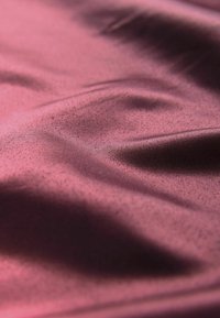 Szatynowa tkanina w głębokim burgundzie, charakteryzująca się gładką teksturą z subtelnym połyskiem i delikatnymi falami, podkreślająca miękkość i płynność.
