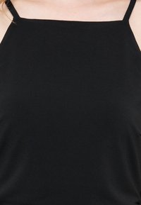 Μαύρο αμάνικο τοπ με λεπτές τιράντες στους ώμους και τετράγωνο ντεκολτέ που φοριέται από άτομο, δείχνοντας το πάνω μέρος του στήθους και τους ώμους.