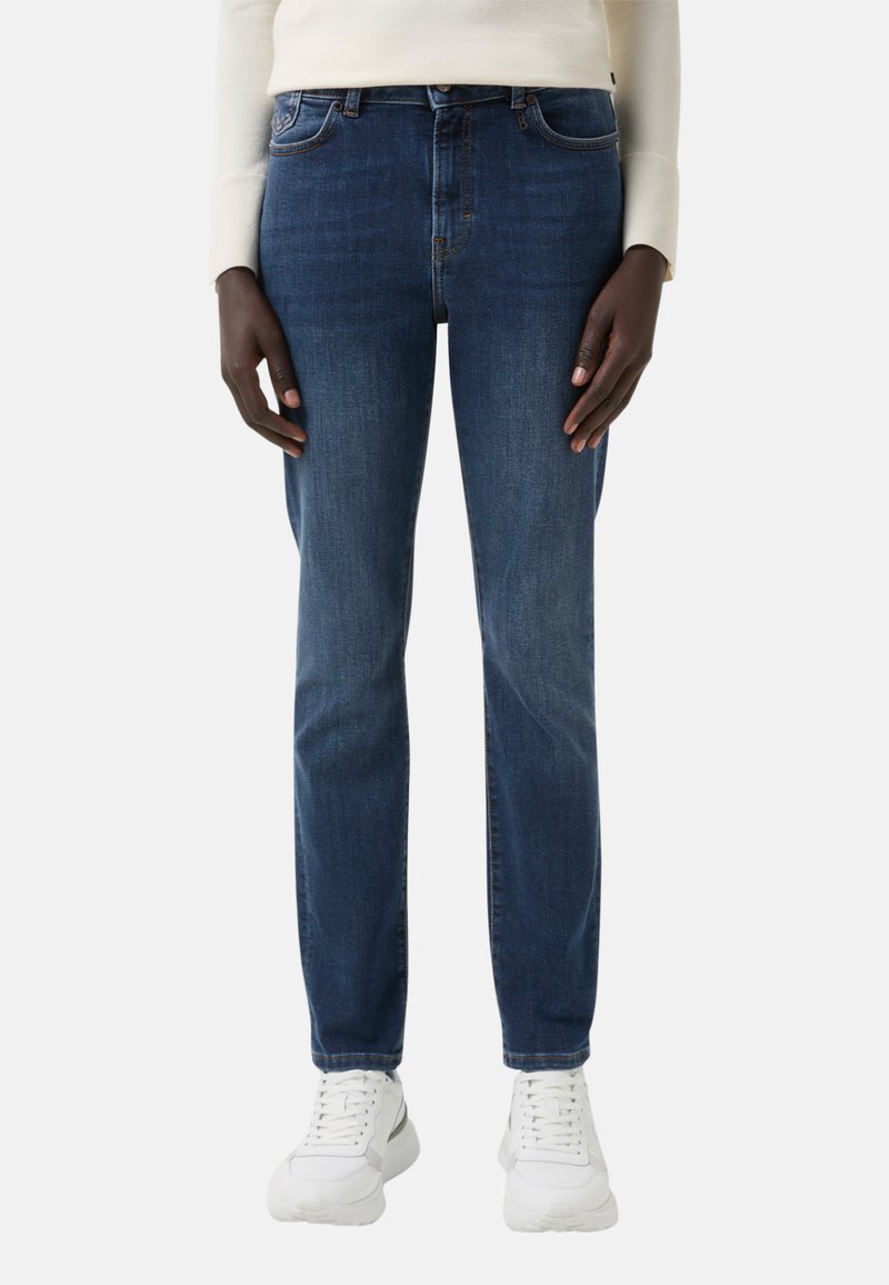 Tmavě modré džínové kalhoty s úzkým střihem, designem s pěti kapsami, s výšivkami jako akcenty. V kombinaci s bílými teniskami.