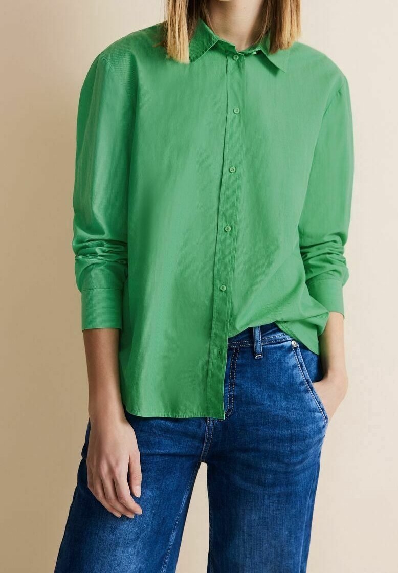 Grön skjorta med knappar, tillverkad av lätt tyg, med krage och lång ärm, ihop med blå denimjeans.
