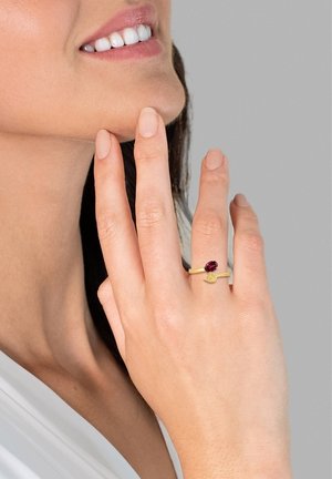 Bague en or avec une pierre rouge centrale et un petit accent décoratif. Finition lisse, design de bande simple, portée à l'index.