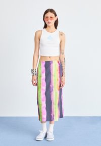 Bijela kratka majica bez rukava s plavim natpisom, uparen s veselim, tie-dye maxi suknjom koja ima ružičaste, zelene i sivo-vertikalne pruge. Bijele tenisice.