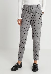 Grijze broek met stippen, voorzien van een trekkoord in de taille en een taps toelopende pasvorm, gecombineerd met zwarte instappers. Soepele stof met een lichte glans.