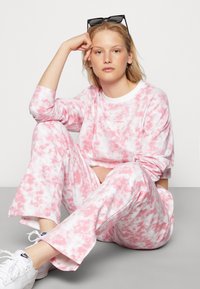 Conjunto de roupa de lazer em tie-dye rosa e branco, apresentando uma blusa de mangas longas e calças combinando, feito de um tecido suave com um corte descontraído.