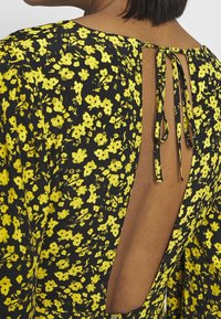 Černé šaty s malými žlutými květinovými vzory, s hlubokým výřezem na zádech a zavazováním na krku. Měkká, lehká textura látky.