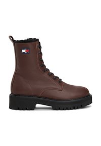 Bota de combate de cuero marrón con acabado texturizado, suela de goma negra con agarre, diseño de cordones y un cuello forrado en forro polar. Presenta un parche con el logo.