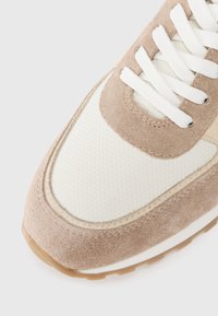 Lys brun nubuck sneaker med en strukturert hvit mesh overlay, hvite snørebånd og en gummigummisåle. Har rund tå og lagdelt design.