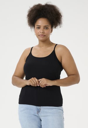 Schwarzes, eng anliegendes Tanktop mit dünnen Trägern. Weicher, dehnbarer Stoff. Das Model trägt hellblaue Jeans, die Hände vor sich gefaltet, steht vor einem weißen Hintergrund.