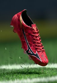 Sarkans futbola kurpes ar ģeometrisko rakstu, melniem akcentiem un saišu. Iezīmējas ar izsmalcinātu dizainu un paaugstinātu izcilnspiedienu zoli, kas nodrošina saķeri.