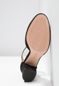 Escarpin en daim noir à talon haut avec une semelle texturée. Présente un design ouvert et une semelle intérieure beige, mettant en valeur la forme raffinée de la chaussure.