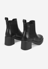 Botas de tobillo de cuero negro con un tacón grueso y cuadrado, paneles laterales elásticos y lengüetas de tirón. Textura suave con un diseño minimalista.