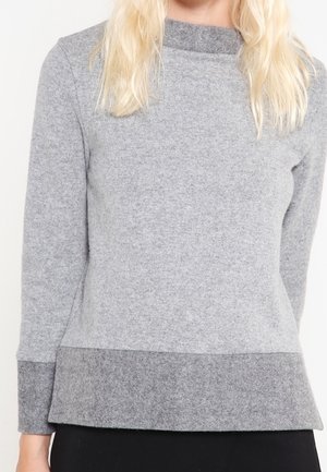 Sudadera gris hecha de una tela suave, con un cuello alto, mangas largas y un dobladillo gris más oscuro en la parte inferior. Diseño sencillo.