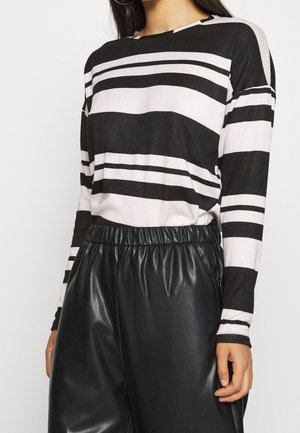 Černobílé pruhované tričko s dlouhým rukávem v kombinaci s černými koženkovými kalhotami s vysokým pasem. Materiál působí měkce a má volný střih.