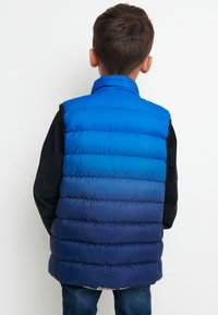 Modrý puffový vest s postupnou barvou od jasně modré na ramenou po tmavě modrou na lemu. Má vysoký límec a prošívaný design.