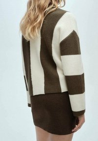Cardigan en tricot à rayures horizontales blanches et brunes, tissu texturé, encolure ronde et poignets côtelés. Associé à une jupe brune.