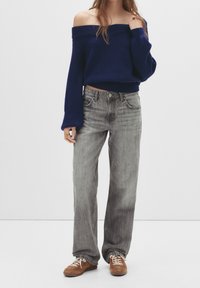 Pull marin côtelé à épaules dénudées, associé à un jean gris clair à jambes larges, et à des baskets en daim marron avec des lacets beige.