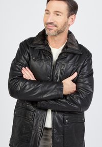 Zwarte leren jas met een zachte, gestructureerde kraag, meerdere voorzakken en drukknopen. Slim fit ontwerp met een gladde afwerking.