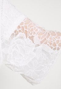 Tessuto di pizzo bianco con motivi floreali, caratterizzato da una texture morbida e un design fluente. I bordi sono smerlati per una finitura delicata.