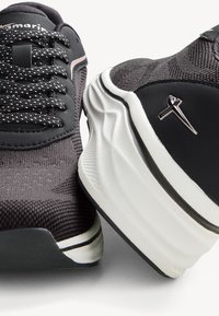 Black athletic shoes with textured knit upper, contrasting white sole, and reflective accents. Features lacing and logo detail on the side.