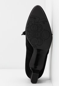 Chaussure à talon haut en daim noir avec un bout pointu. La semelle présente des motifs embossés complexes ainsi que le nom de la marque "PETER KAISER."