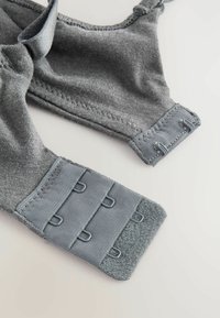Sutien din material gri, cu bretele reglabile, închidere cu unde și ochi, și textură netedă. Prezintă cusături plate și accesorii rezistente pentru suport.