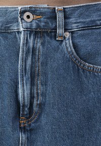 Modri jeans iz denima z kontrastnim oranžnim šivom, kovinskim gumbom za zapiranje in sprednjimi žepi z rahlo zbledelim videzom.