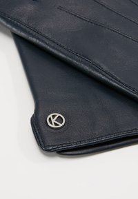 Guanti in pelle blu marino con dettagli cuciti e un accento circolare in argento. La pelle presenta una texture liscia e una finitura raffinata.