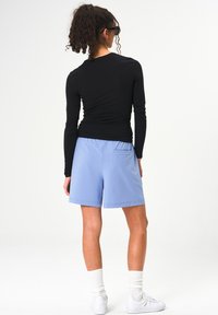 Schwarzes Langarmshirt und hellblaue Shorts mit elastischem Bund, ausgestattet mit einer Gesäßtasche und weißen Sportsocken.