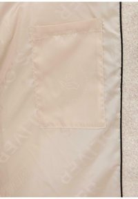 Intérieur en tissu beige clair avec une poche. Présente des instructions d'entretien en relief et un graphique d'une main avec un cœur. Texture douce.