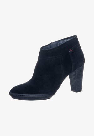 Černá semišová kotníková bota s vysokým zúženým podpatkem a jemným červeným a modrým prošitím po straně.