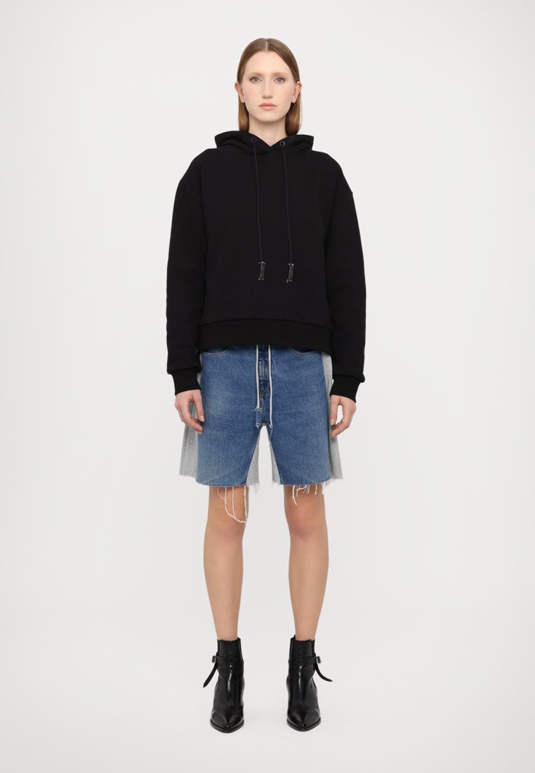 Haut de hoodie noir court avec cordons, associé à un short en denim bleu avec des bords effilochés. Porté avec des bottines noires coupe cheville.