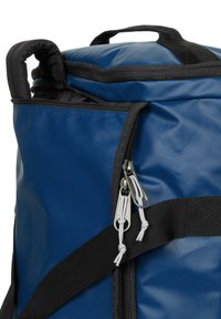 Blaues wasserdichtes Tasche mit schwarzen Akzenten, ausgestattet mit einem Reißverschlussöffnung, einem stabilen Handgriff und einem verstellbaren Riemen.