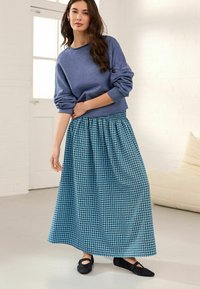 Felpa blu con maniche arrotolate abbinata a una lunga gonna maxi a scacchi blu e verde; ballerine nere completano l'outfit.