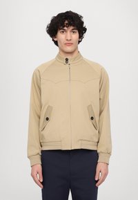 Béžová bunda na zip s vyvýšeným límcem, bočními kapsami a žebrovanými manžetami. Obsahuje prošité detaily a přiléhavý střih.