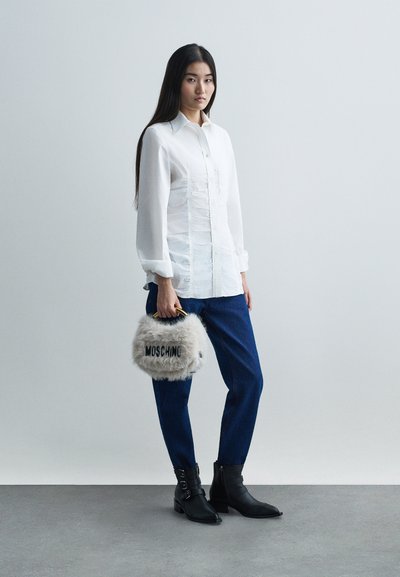 Witte, knoopjesoverhemd met geplooide details, blauwe jeans, zwarte enkellaarsjes en een fluffy grijze Moschino-handtas met een zwart logo.