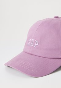 Rosa bomull-baseballcap med buet skygge og brodert "GAP"-logo på forsiden. Har et teksturert stoff og justerbar stropp.