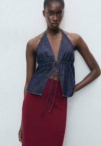 Top in denim con scollo all'americana e vita cinata, abbinato a una gonna a coste bordeaux aderente. Il tessuto ha una consistenza liscia.