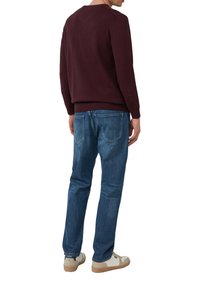 Burgunderfarbener Rundhalsausschnitt-Pullover, kombiniert mit blauen Jeans und weißen Sneakern mit beigen Sohlen. Glatte Textur und lässige Passform.