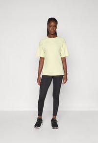 Geel sport t-shirt met korte mouwen, gecombineerd met zwarte legging. Het shirt heeft een subtiel logo en contrasterende naden. Zwarte sneakers maken de look af.
