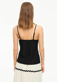 Camiseta negra sin mangas con tirantes finos, tejido texturizado y un diseño ajustado. La parte posterior presenta una superficie lisa y un ligero fruncido en la cintura.