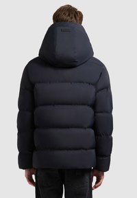 Tengerészkék pufi dzseki magas gallérral és nagy kapucnival. Vízszintes varratokkal és sima textúrával rendelkezik. Minimális logó a hátoldalon.