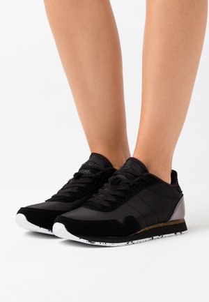 Czarne sneakersy z połączeniem gładkich i teksturowanych materiałów, z białą podeszwą w kropkowany wzór oraz metalicznymi akcentami.