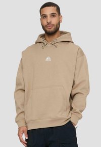 Felpa con cappuccio beige con tasca frontale, coulisse regolabile e un piccolo logo argentato sul petto. Tessuto morbido con vestibilità comoda.